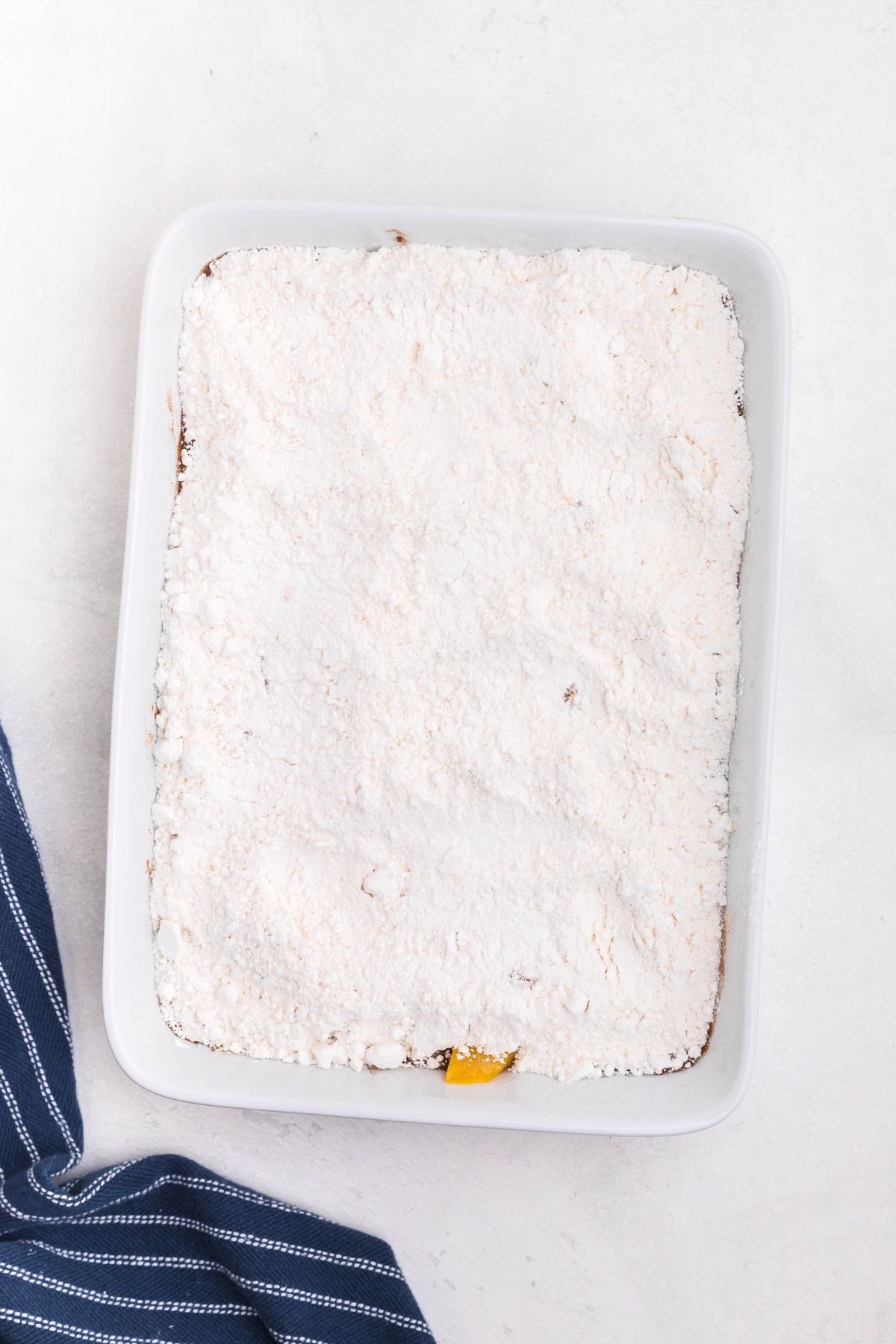 Cake mix powder, spread out over peaches, in a a white rectangle dish. 