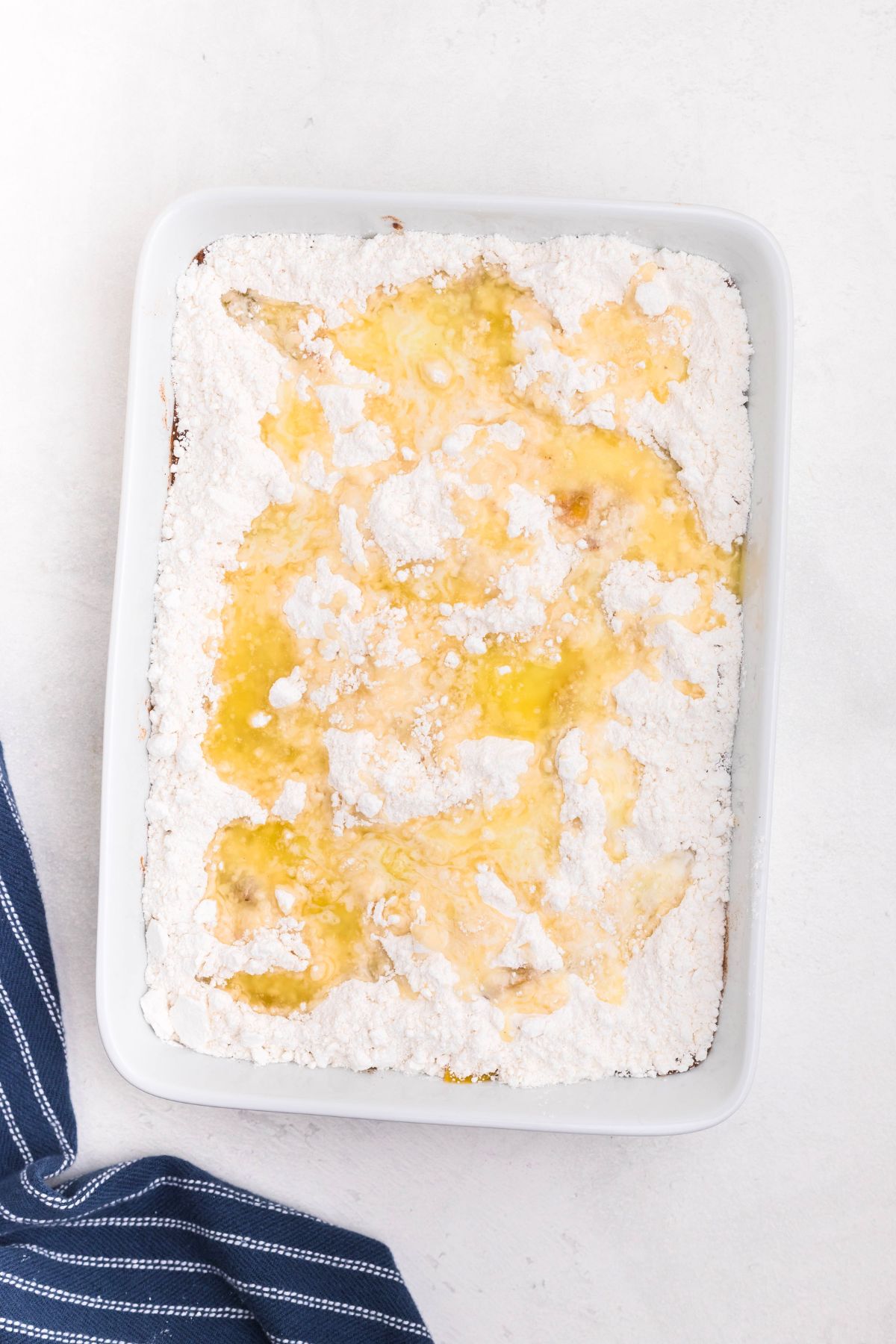Peaches in a white rectangle dish, covered in box cake mix, drizzled with melted butter. 