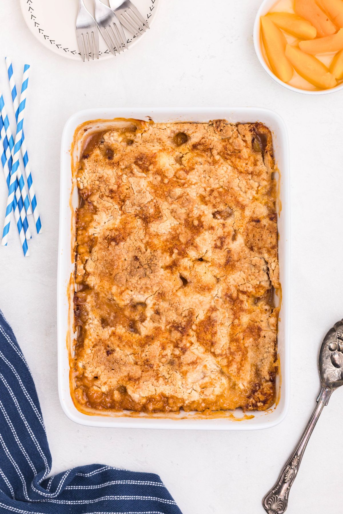 Peaches in a white rectangle dish, covered in box cake mix, drizzled with melted butter, then baked until golden brown and bubbly. 