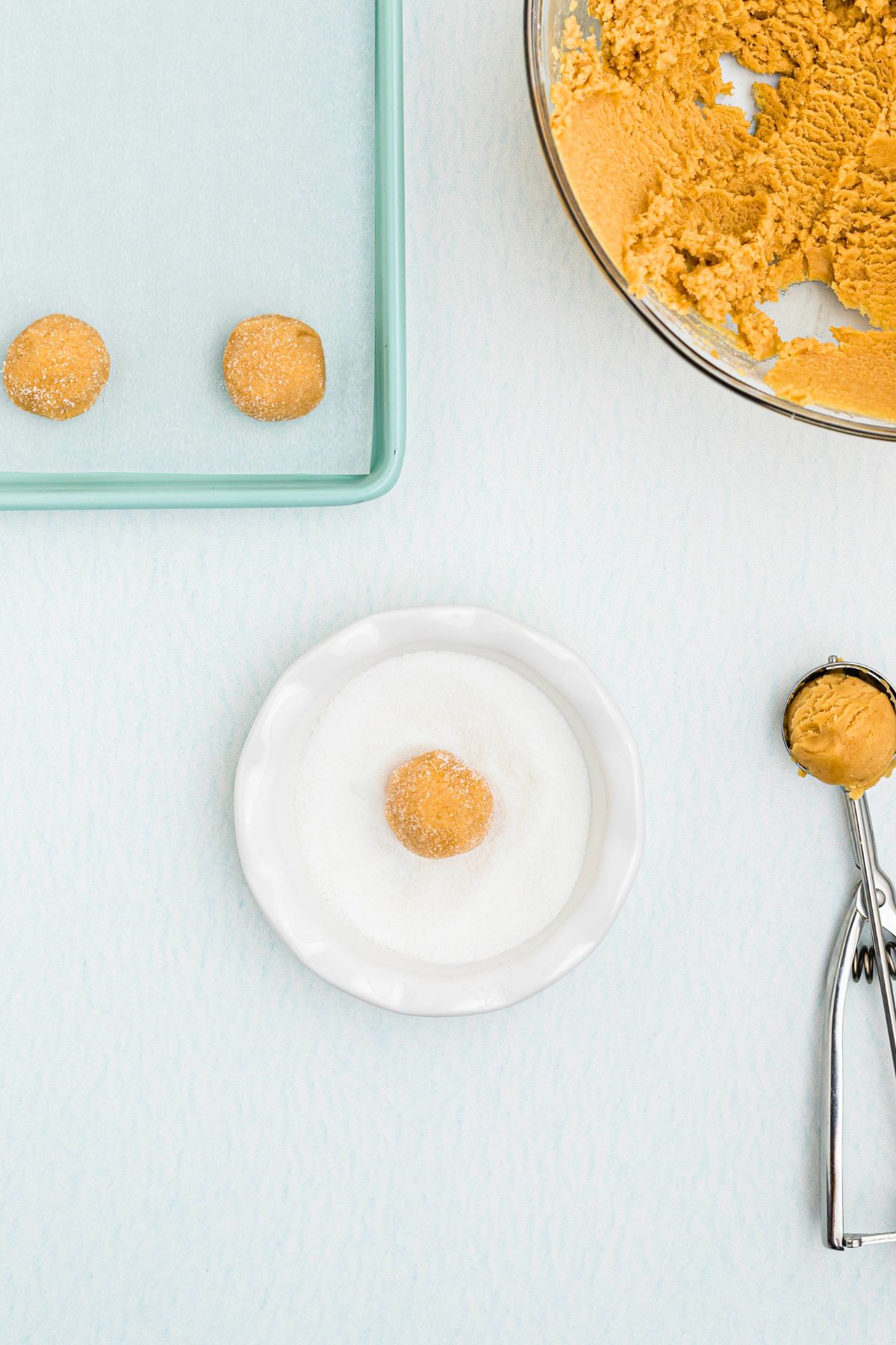 Balls of peanut butter dough being rolled in sugar and placed on baking sheet. 