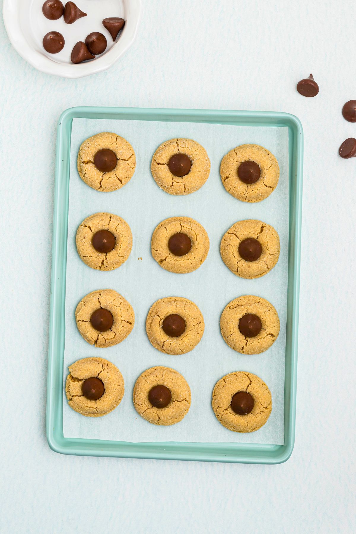 Peanut Butter cookies on a baking sheet, lined with parchment paper, after being baked, then topped with Hershey's chocolate kisses. 