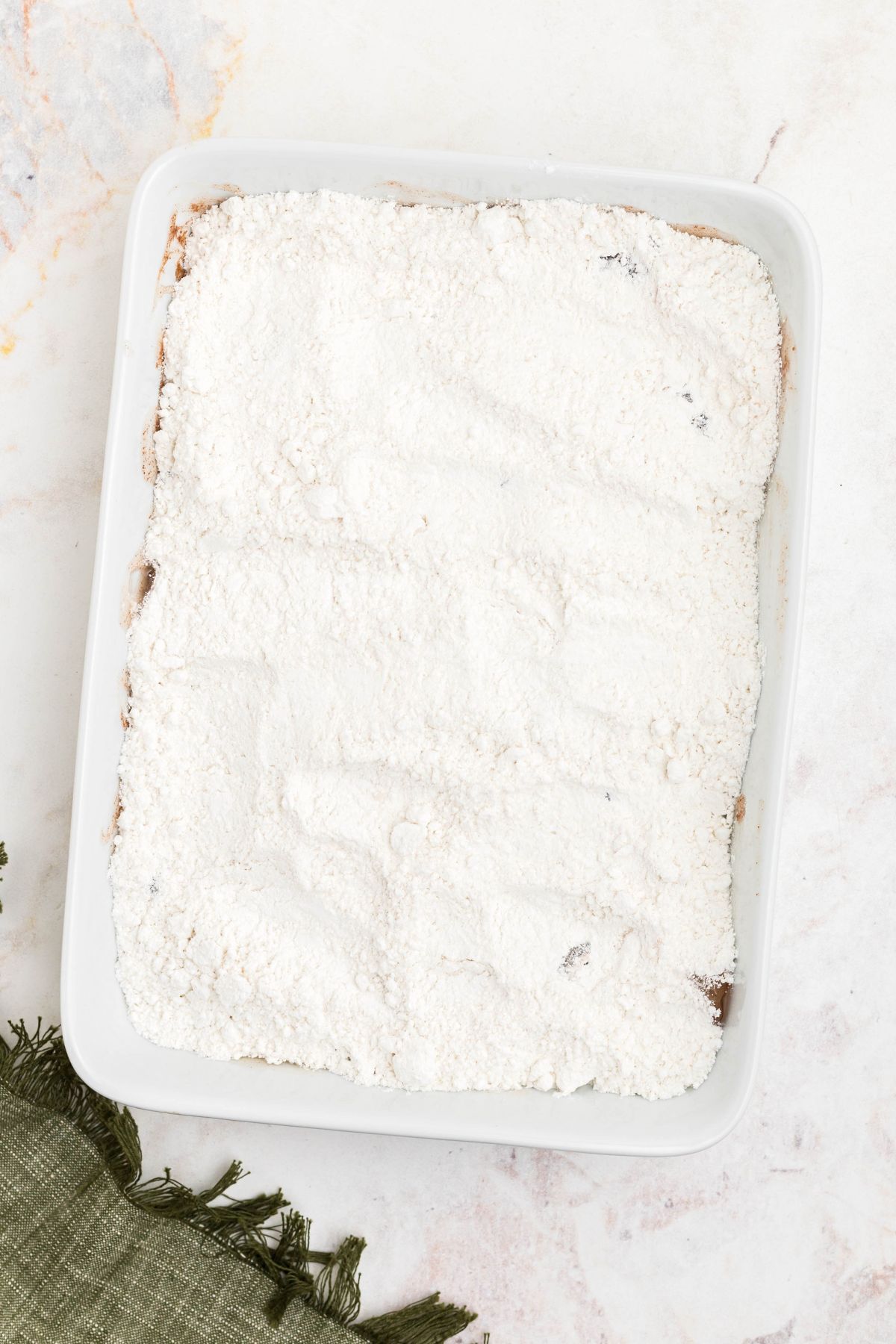 Yellow cake mix poured over pie filling in a white dish, without being stirred together. 