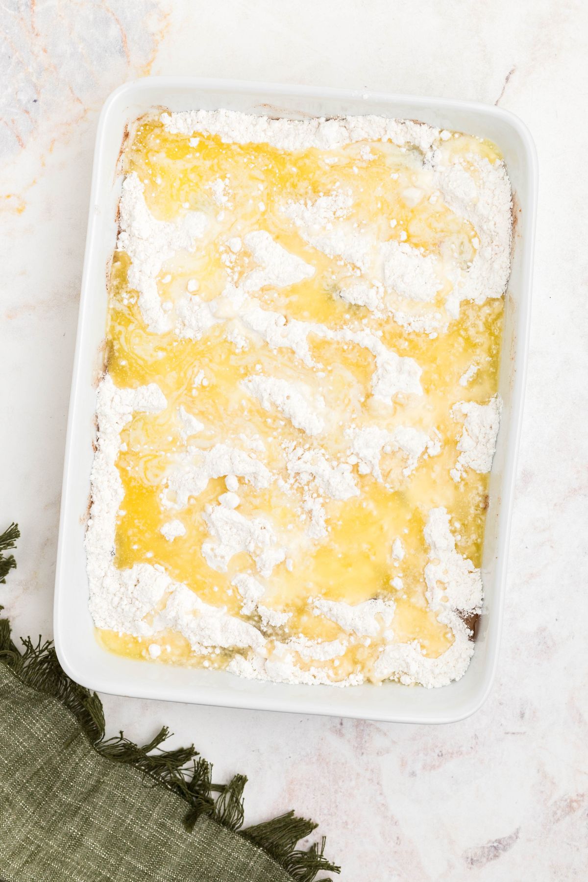 Melted butter drizzled on top of uncooked cake mix powder over apple pie filling in a white baking dish. 