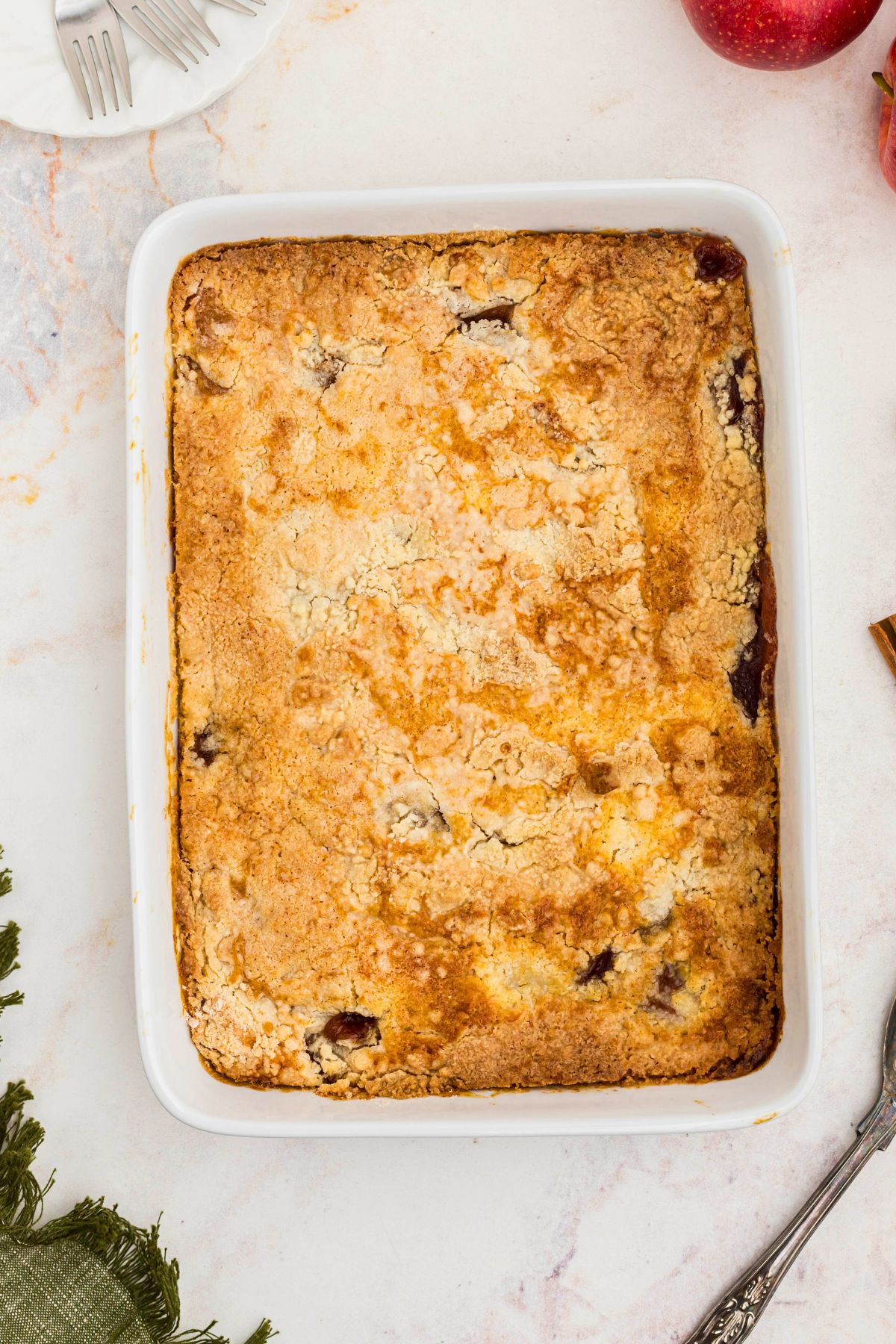 Golden brown crusted apple dump cake in a white baking dish on a marble table. 