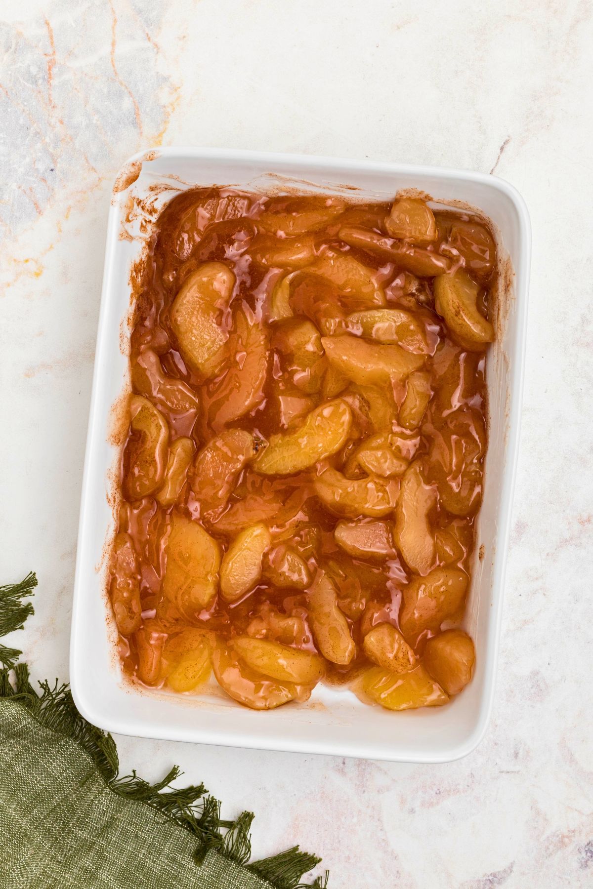 Apple pie filling and ground cinnamon mixed together in a white 9x13 baking dish. 