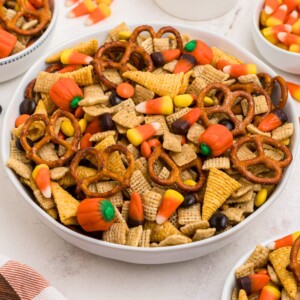Large white bowl filled with Chex mix, pretzels, candy corn, and candies, with some scattered around the table.