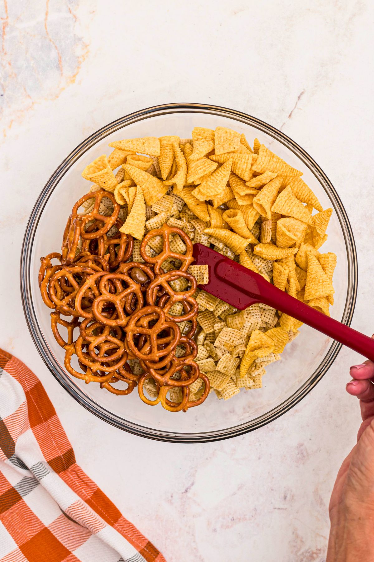 Melted butter and brown sugar mixed with cereal, pretzels, and bugle chips, in a large clear glass mixing bowl. 