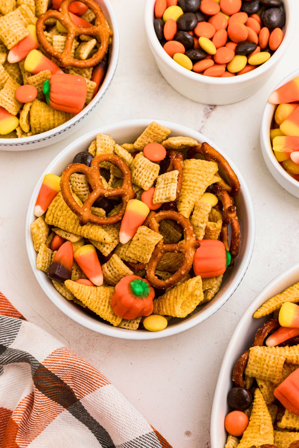 Chex mix cereal, pretzels, candies, and other ingredients, mixed together, and served in small bowls on a marble table. 