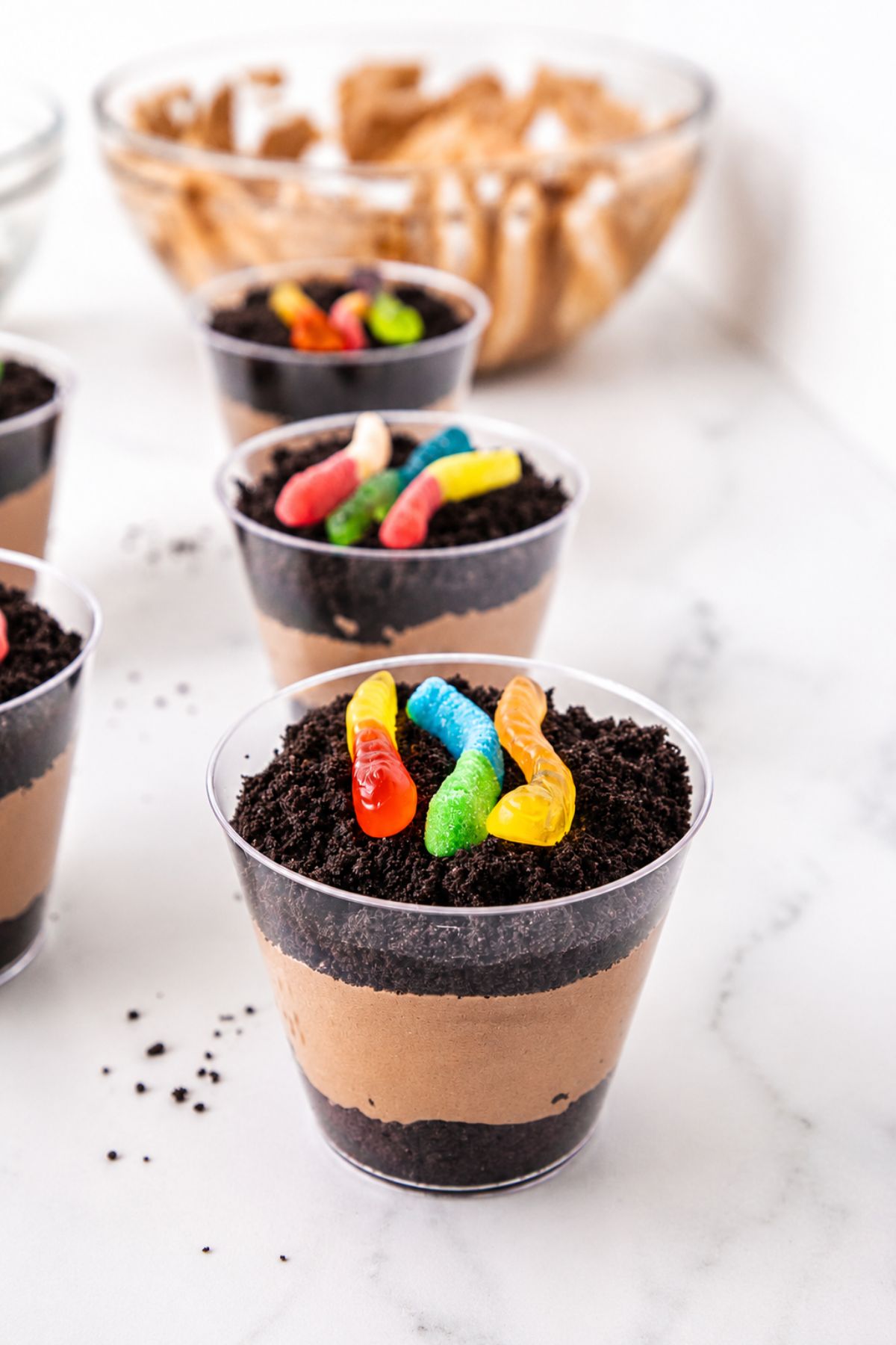 Individual cups filled with layers of crushed cookies, pudding, and then topped with gummy worms.
