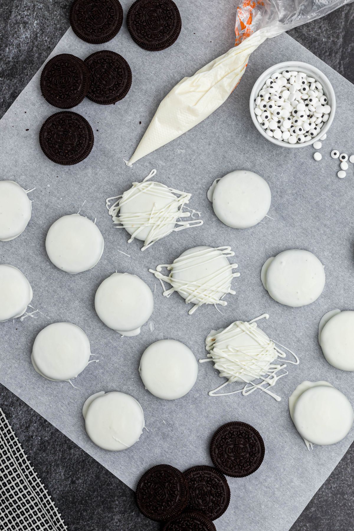 Oreos dipped in white chocolate, drying on parchment paper, with Oreos scattered on the table.