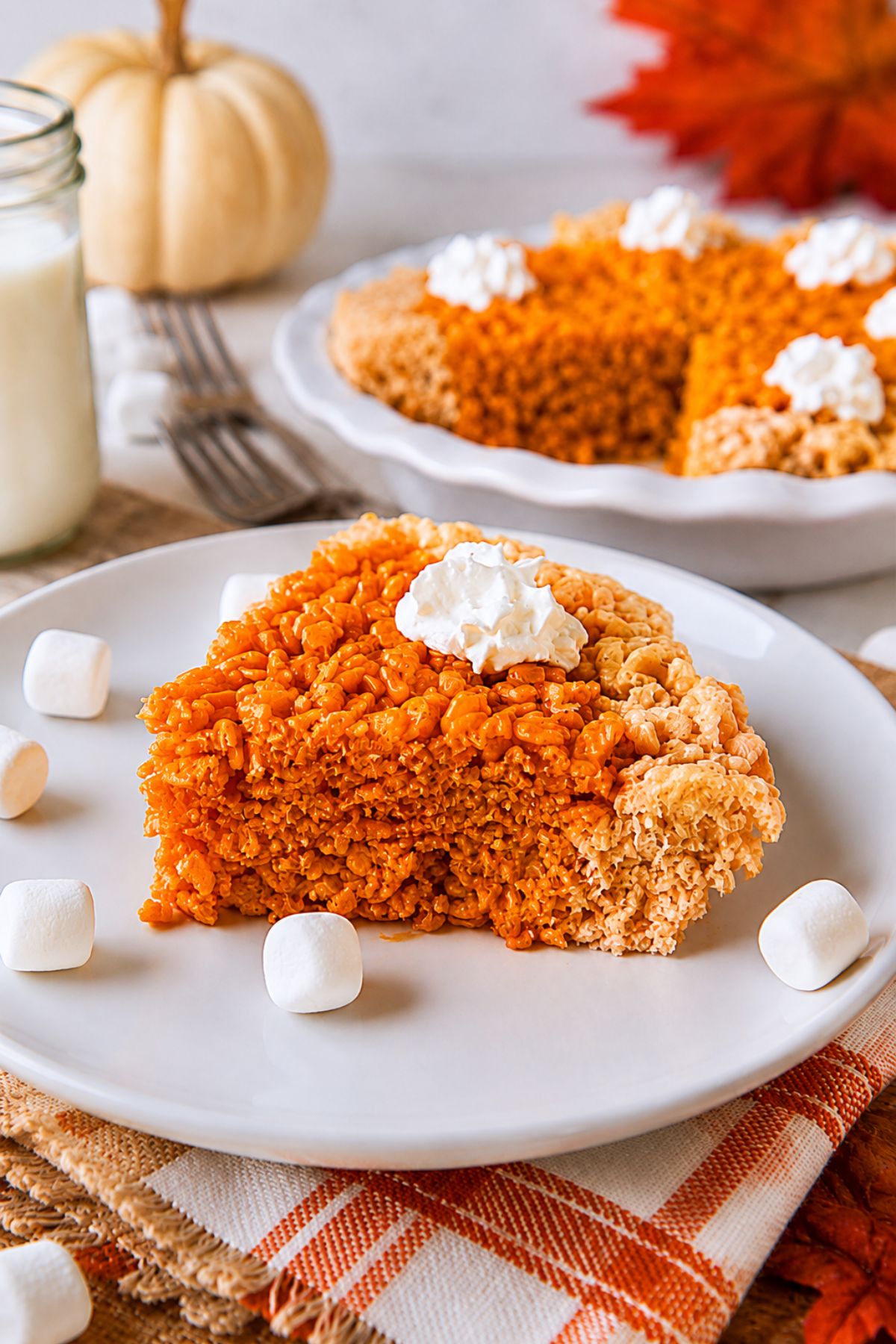 Slice of rice krispie treats shaped like a pumpkin pie, with a topping of whipped cream, on a small white plate.