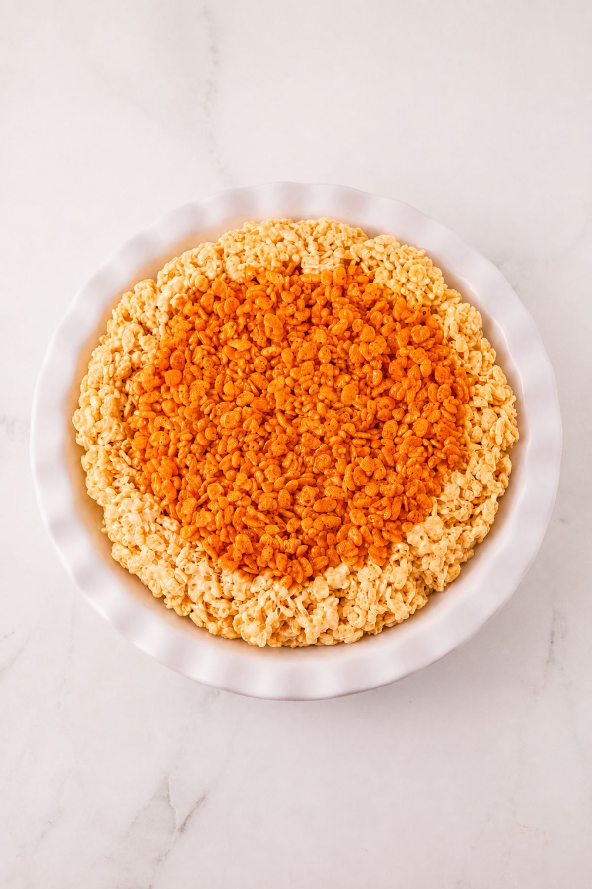 Whole pie of krispie treats in a pie plate, before cutting, on a marble table.