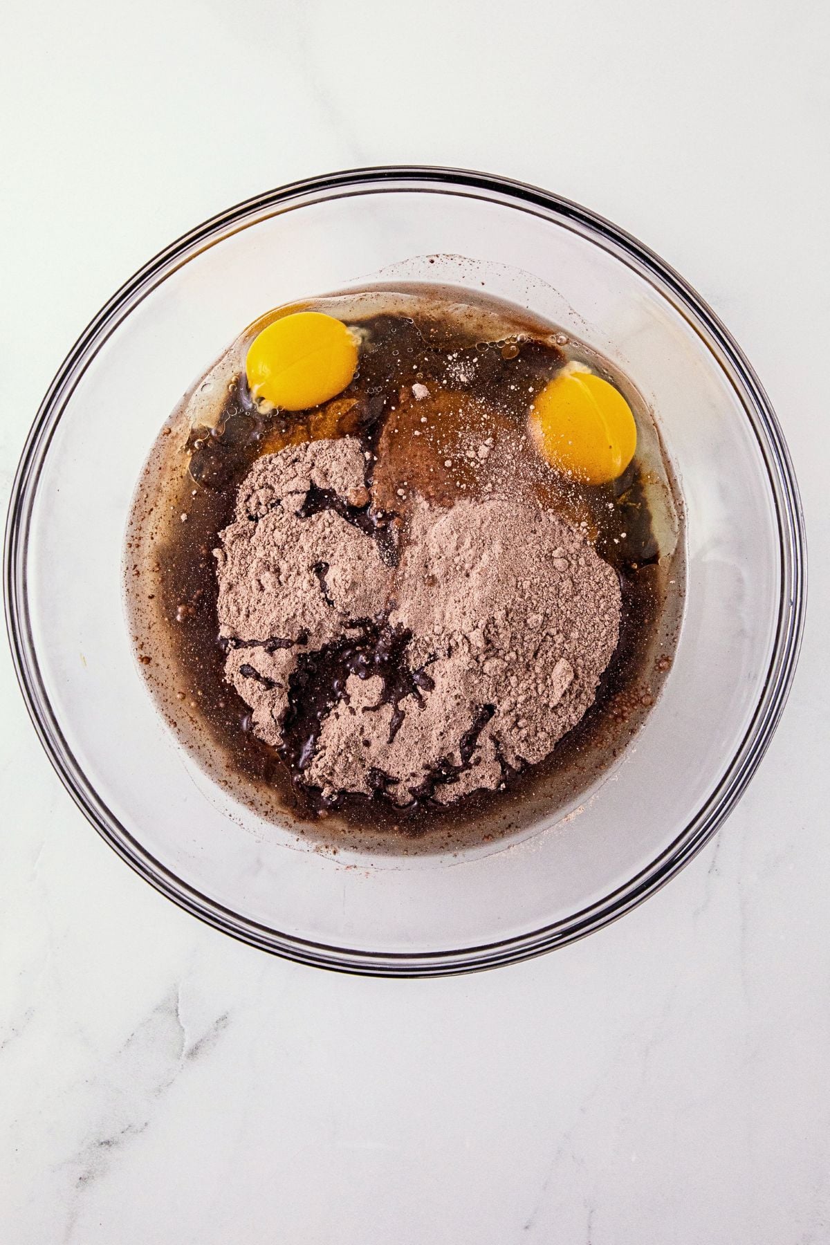 Chocolate cake mix, eggs, and oil, in a large clear glass mixing bowl.