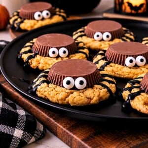 Black plate filled with spider cookies with Halloween decorations on the table.