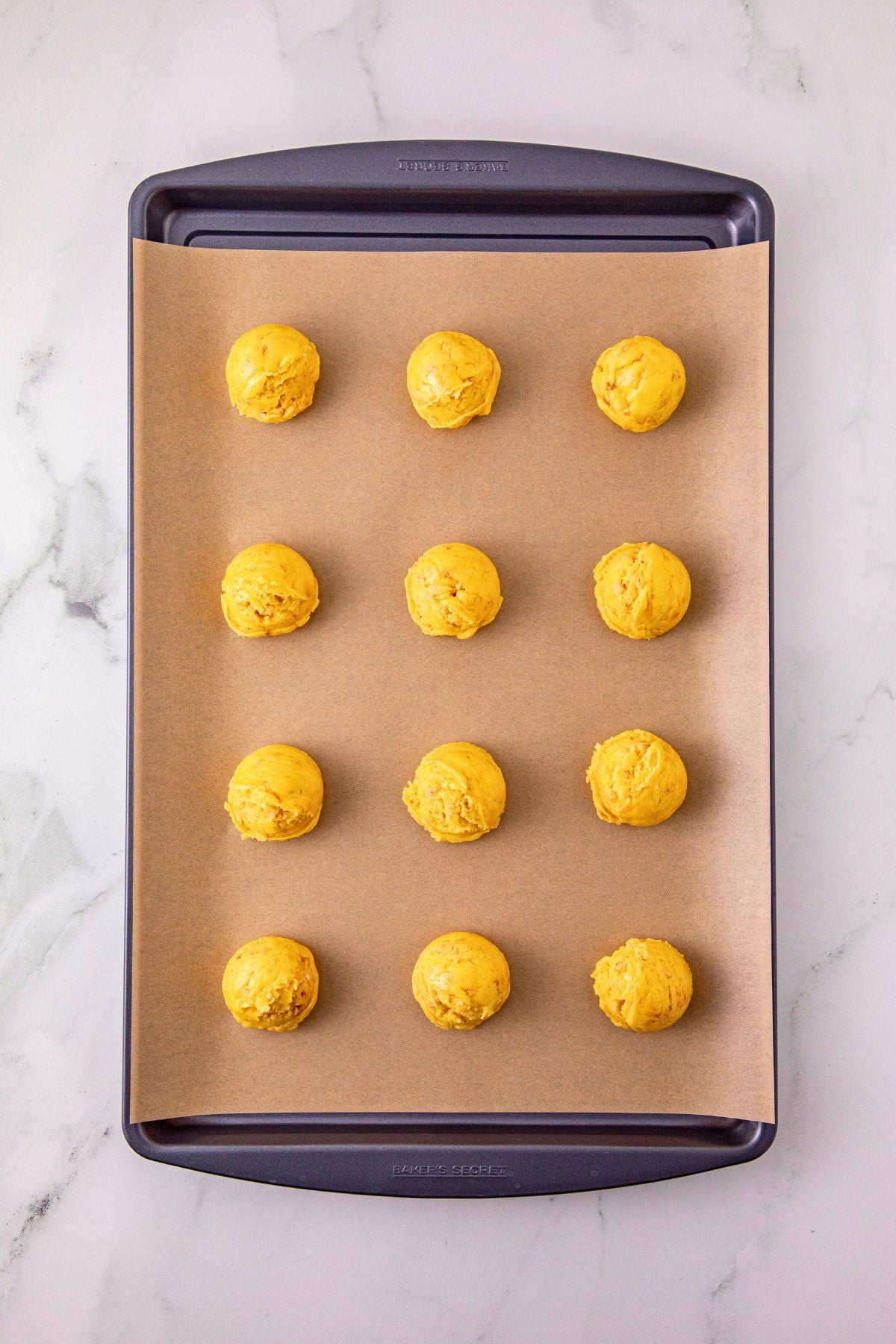 Scoops of dough on a baking sheet, lined with parchment paper. 