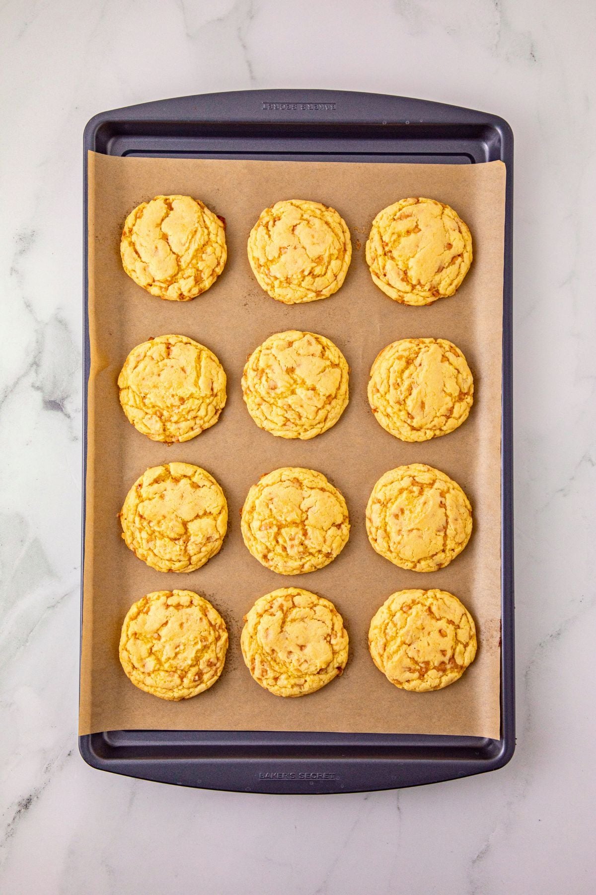 Baked cookies on a baking sheet lined with parchment paper, on a marble table. 