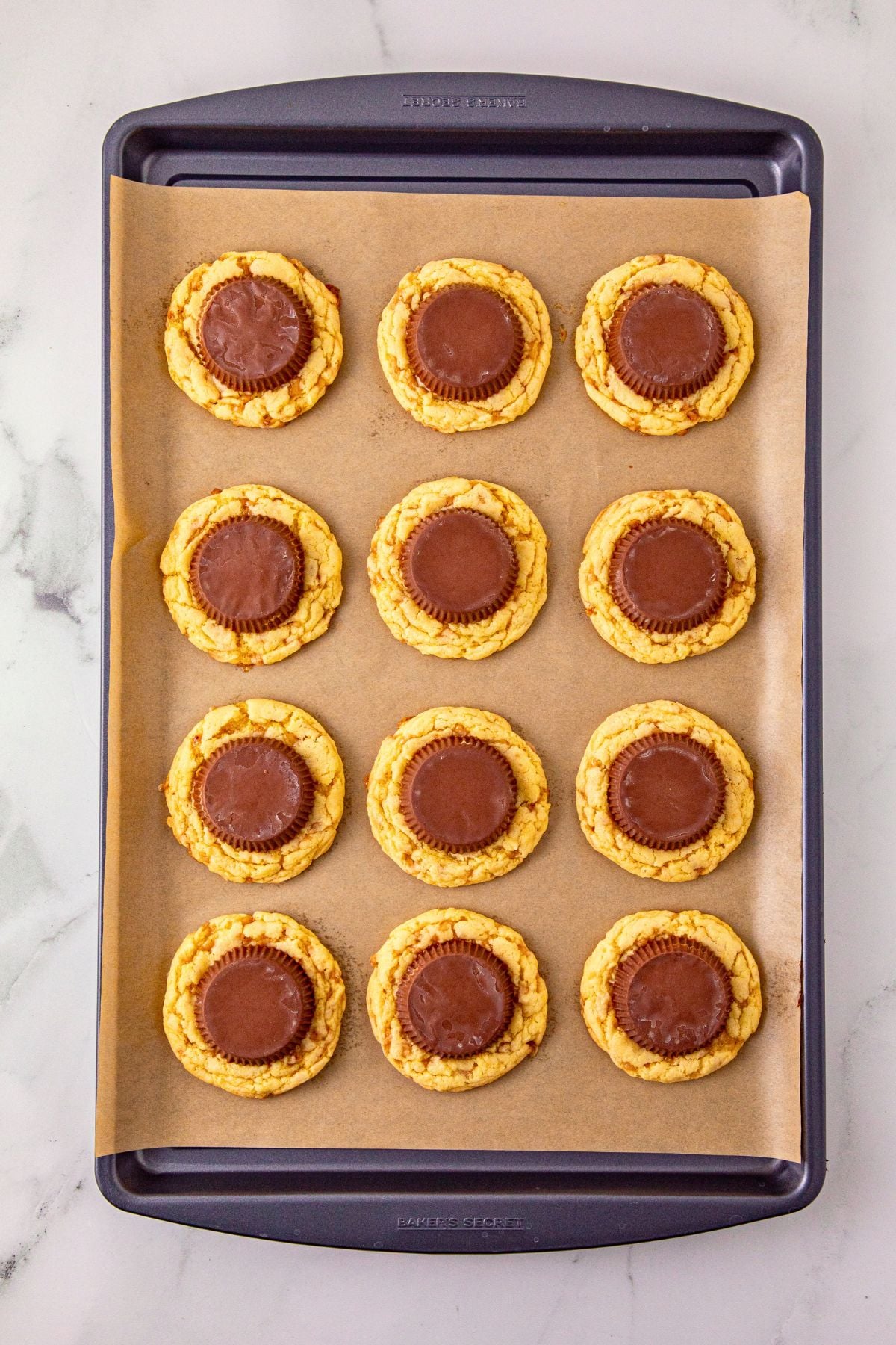 Vanilla cake mix cookies on a baking sheet, topped with peanut butter cup. 