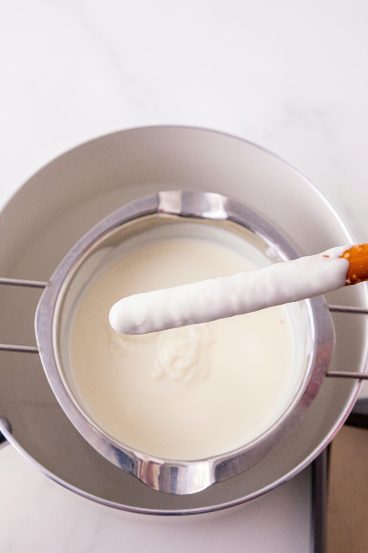 White chocolate melts, melted in a pan, and stirred until smooth and creamy, with a pretzel rod being dipped into the melted coating.