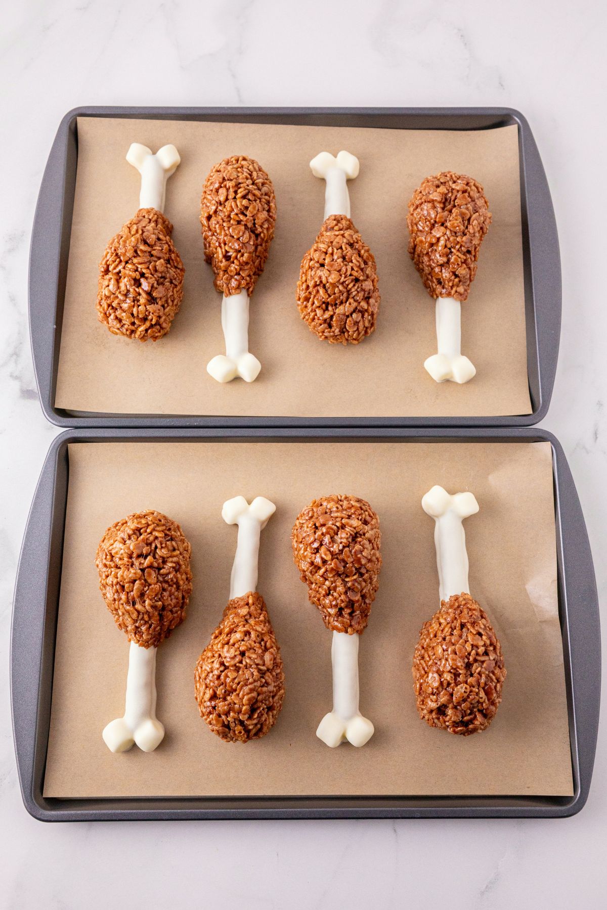 Dipped pretzels, with cocoa krispies, shaped into drumsticks, on a parchment paper lined baking sheet. 