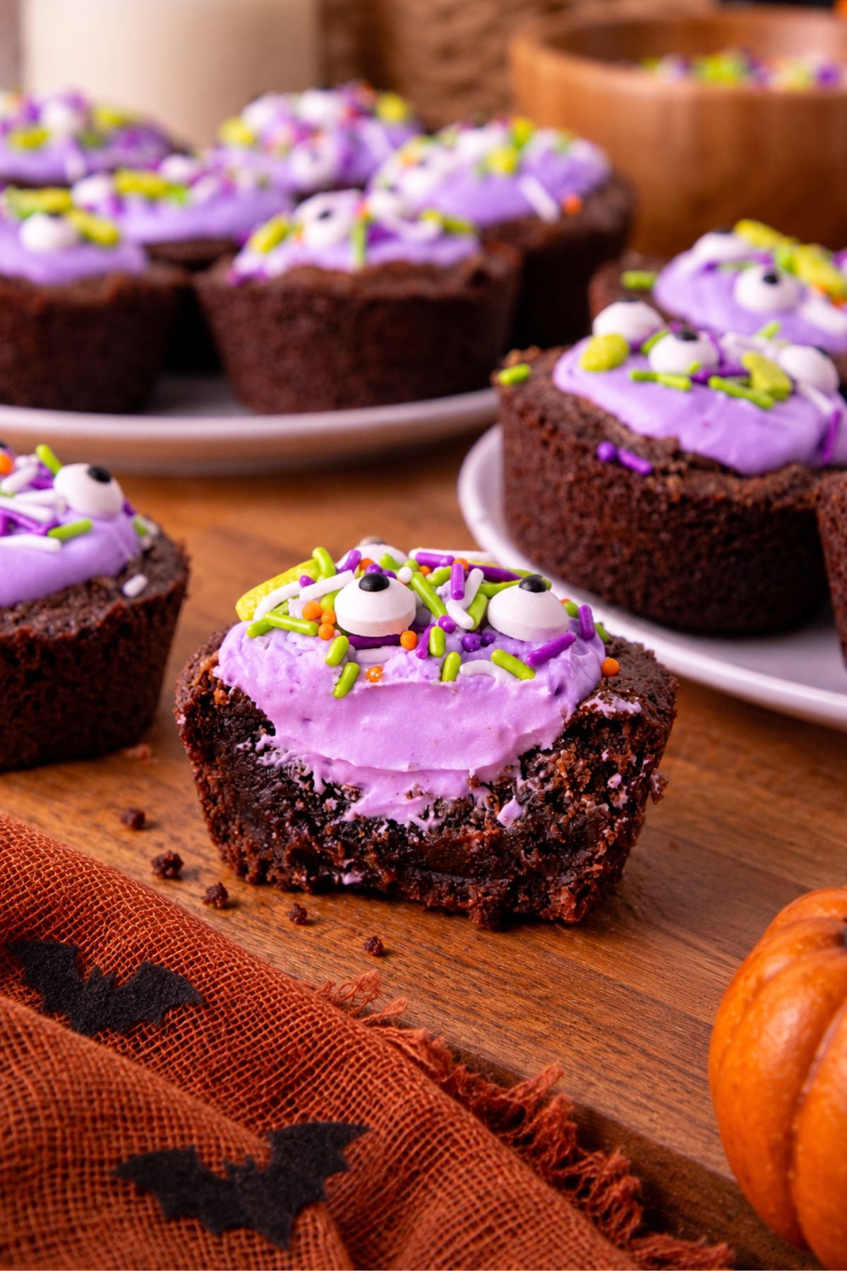 Brownie bites filled with purple frosting and topped with Halloween sprinkles, on a wooden board.