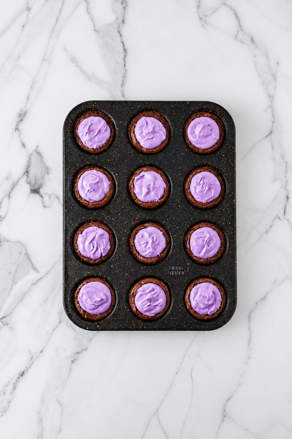 Brownie bites filled with purple frosting in a muffin pan.