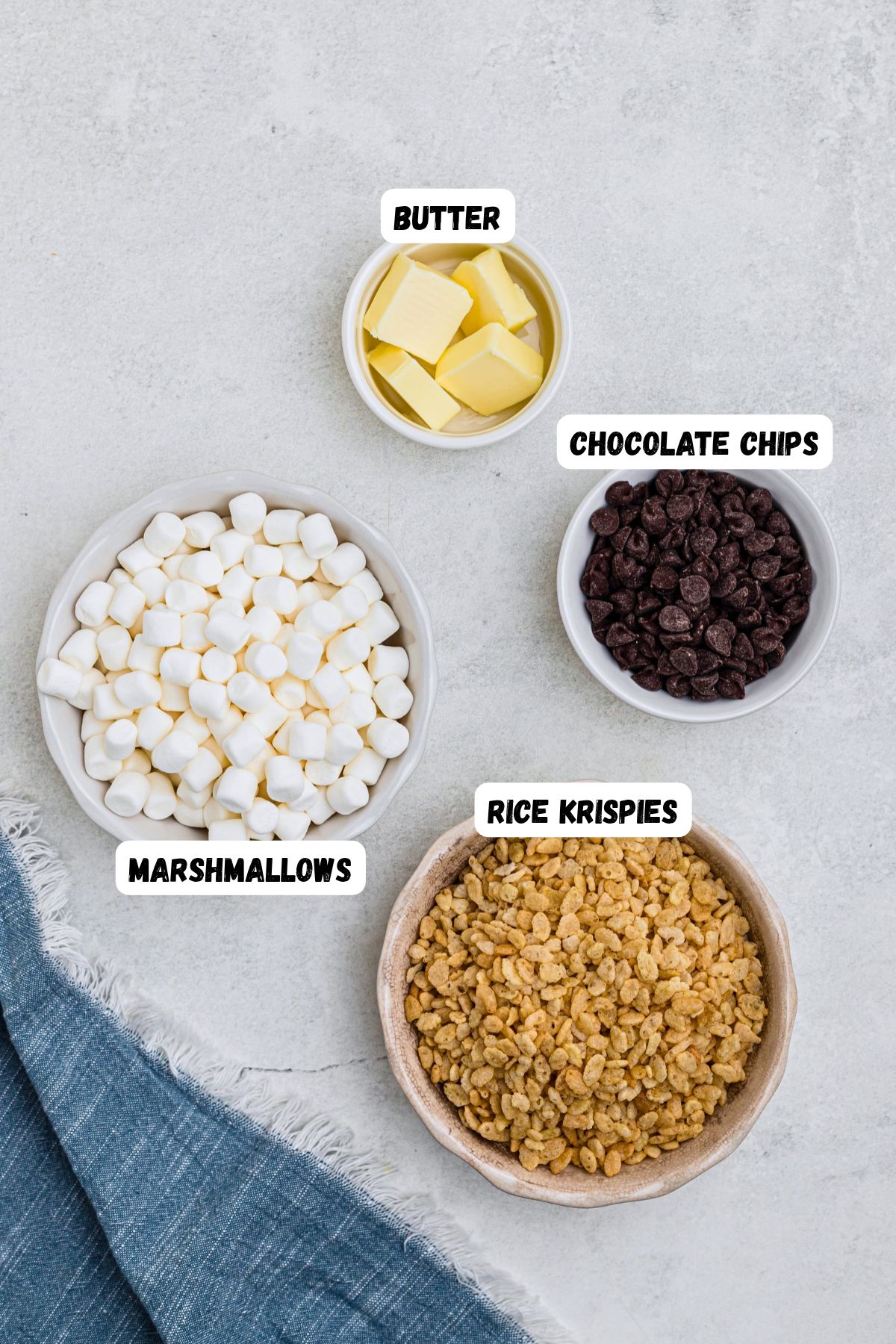 Chips, marshmallows, cereal, and butter, measured and labeled on a marble table. 