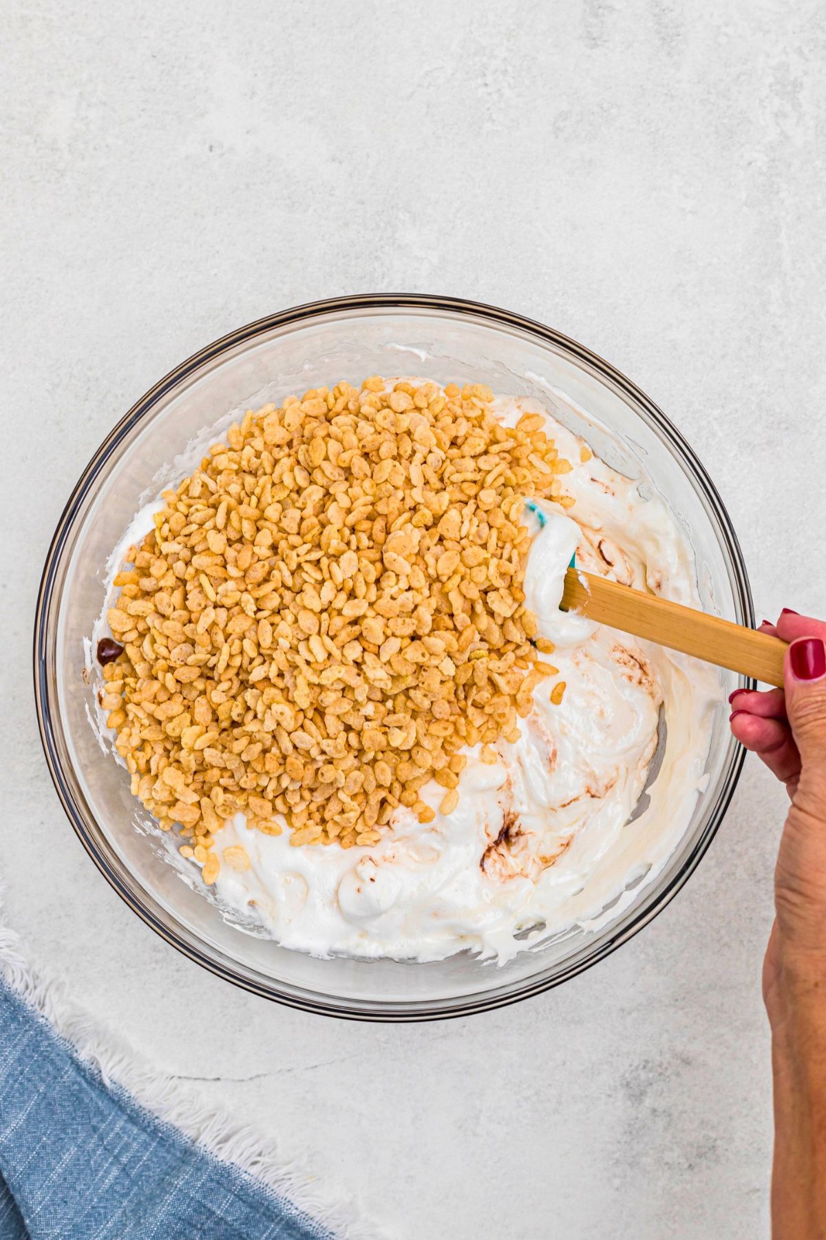 Cereal added to large glass bowl with melted marshmallows, butter, and chocolate chips. 