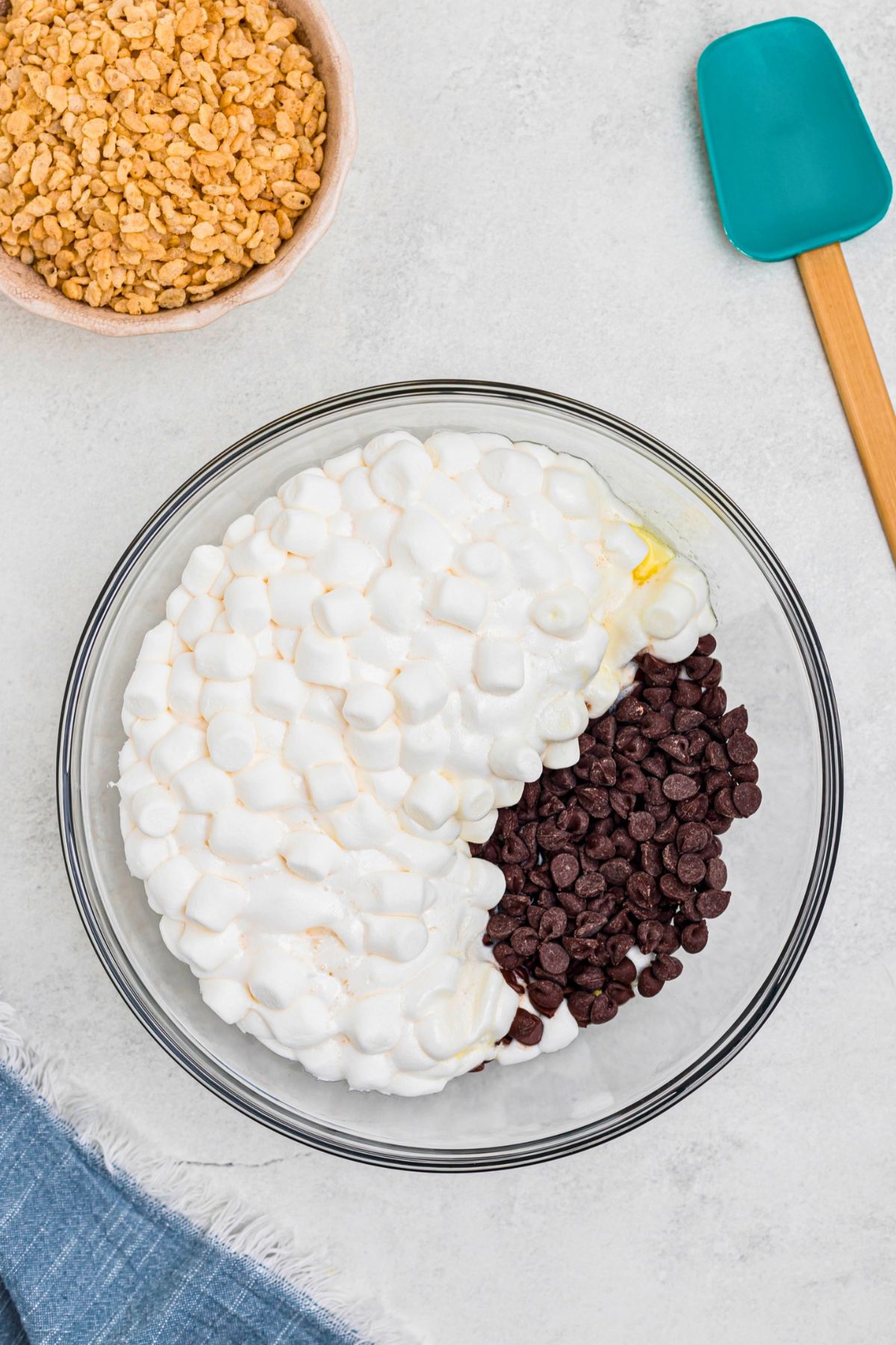 Chips, marshmallows, and butter, in a large clear glass bowl after being microwaved until melted. 