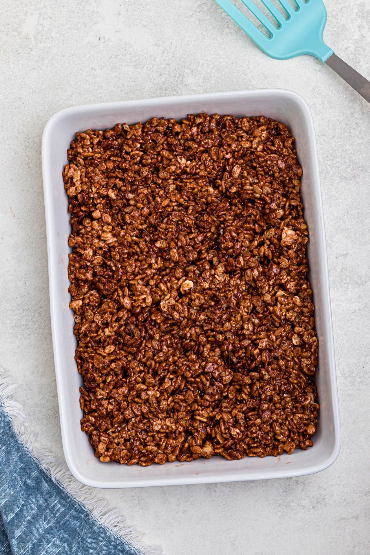 Chocolate rice krispie treats pressed into a white pan before cutting. 