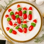 Cherry tomato, basil leaves, and mozzarella pieces on wooden skewers on a white plate, with Christmas decor around the table.