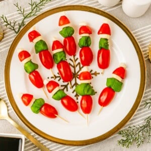 Cherry tomato, basil leaves, and mozzarella pieces on wooden skewers on a white plate, with Christmas decor around the table.