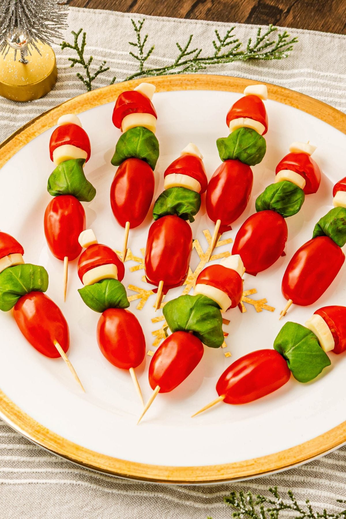 Cherry tomato, basil leaves, and mozzarella pieces on wooden skewers on a white plate, with Christmas decor around the table.