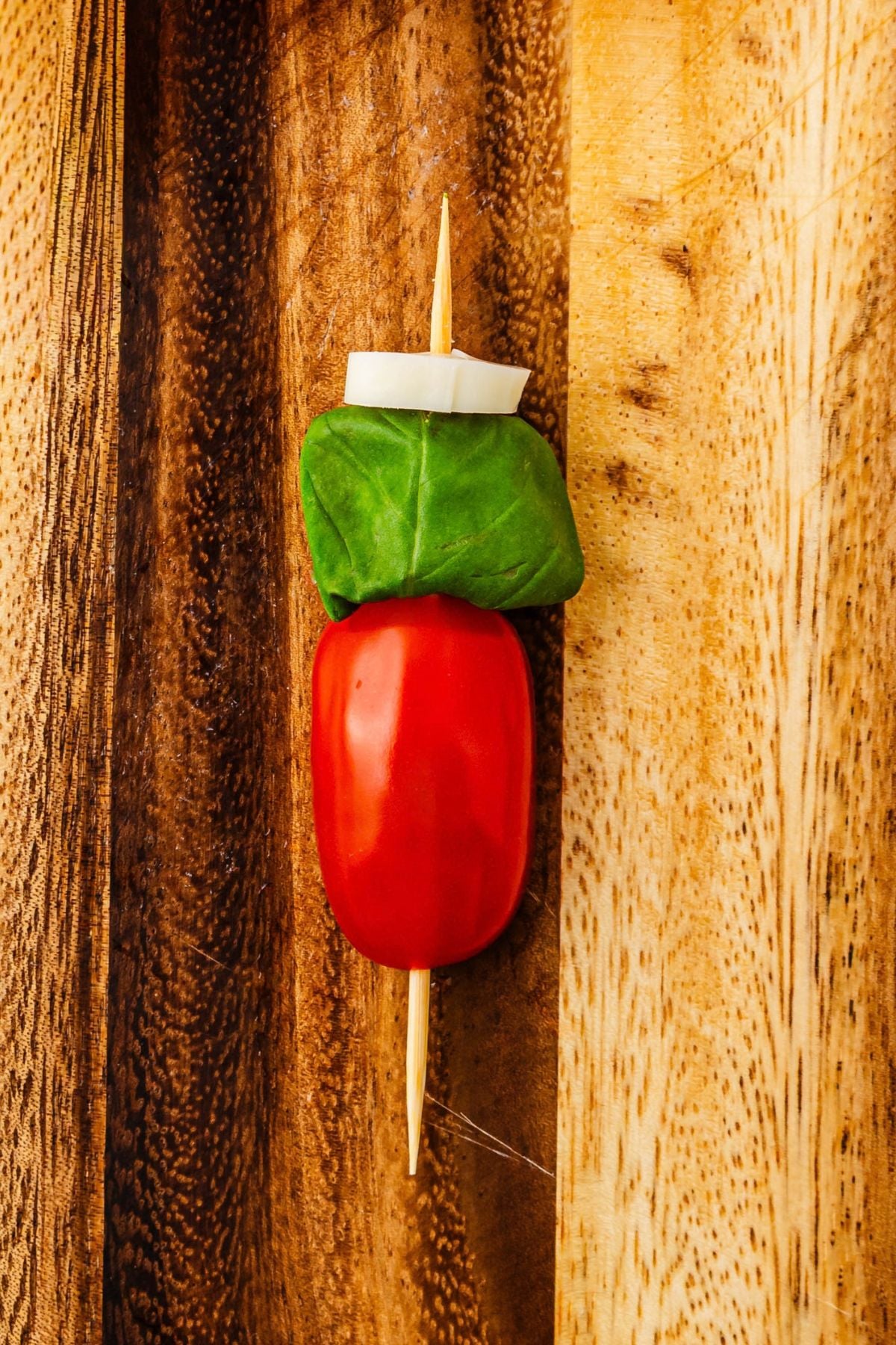 Cherry tomato topped with basil leaf and string cheese piece on a skewer.
