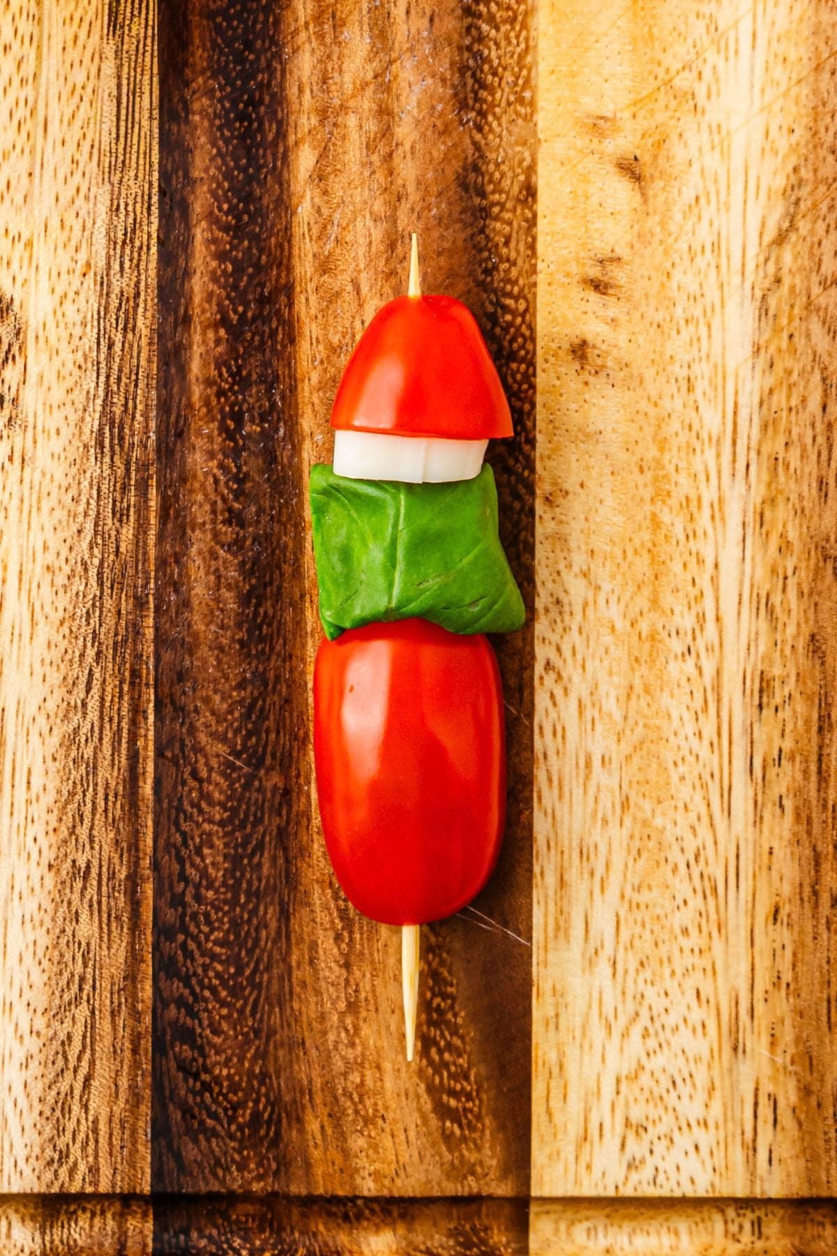 Cherry tomato topped with basil leaf, string cheese piece, and cherry tomato half, on a wooden skewer.
