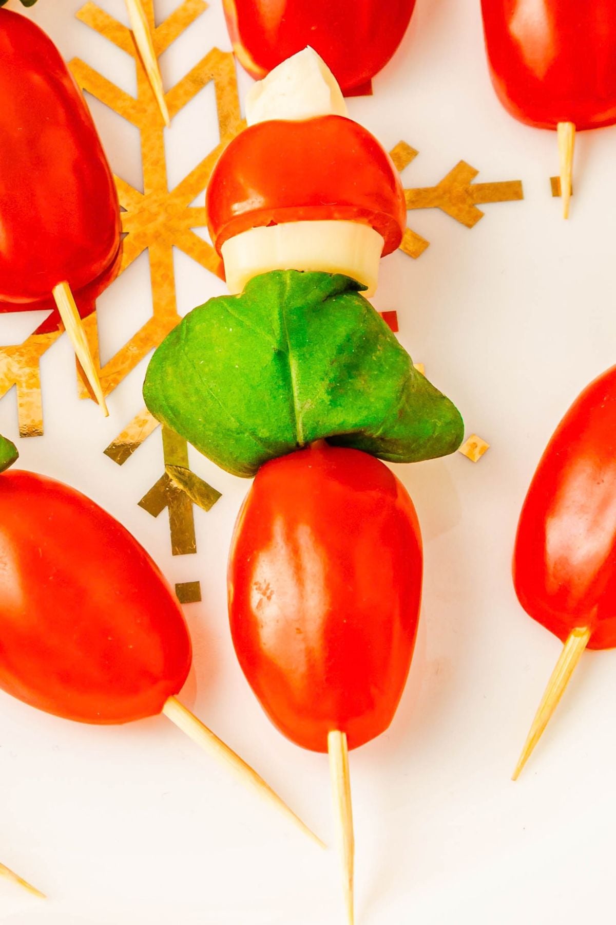 Close picture of mini tomatoes, basil leaves, and mozzarella pieces, on a wooden skewer.