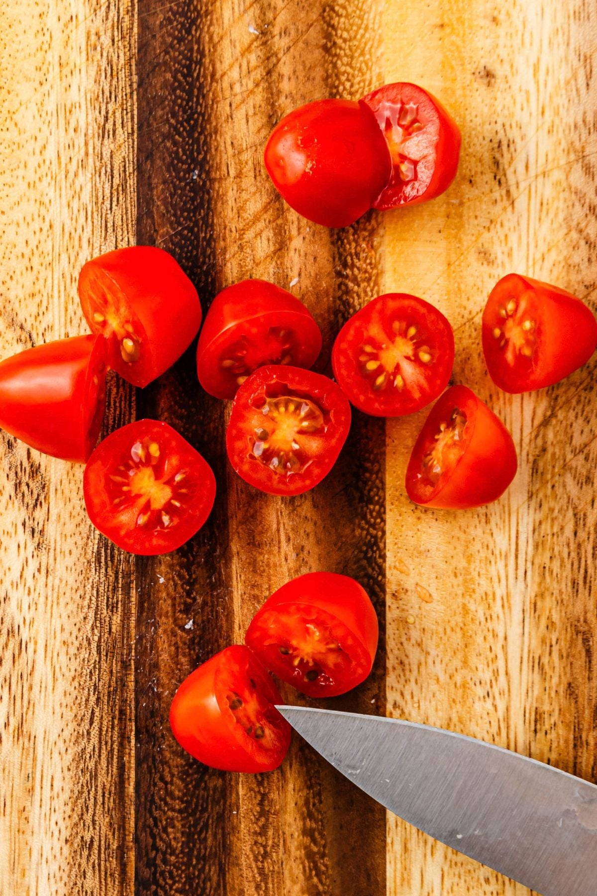 Cherry tomatoes cut in half on a wooden cutting board.