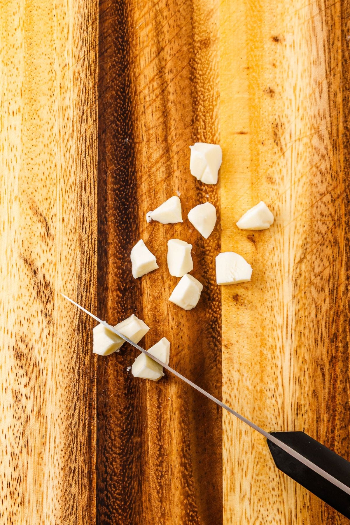 Mozzarella pearls cut in half on a wooden cutting board.