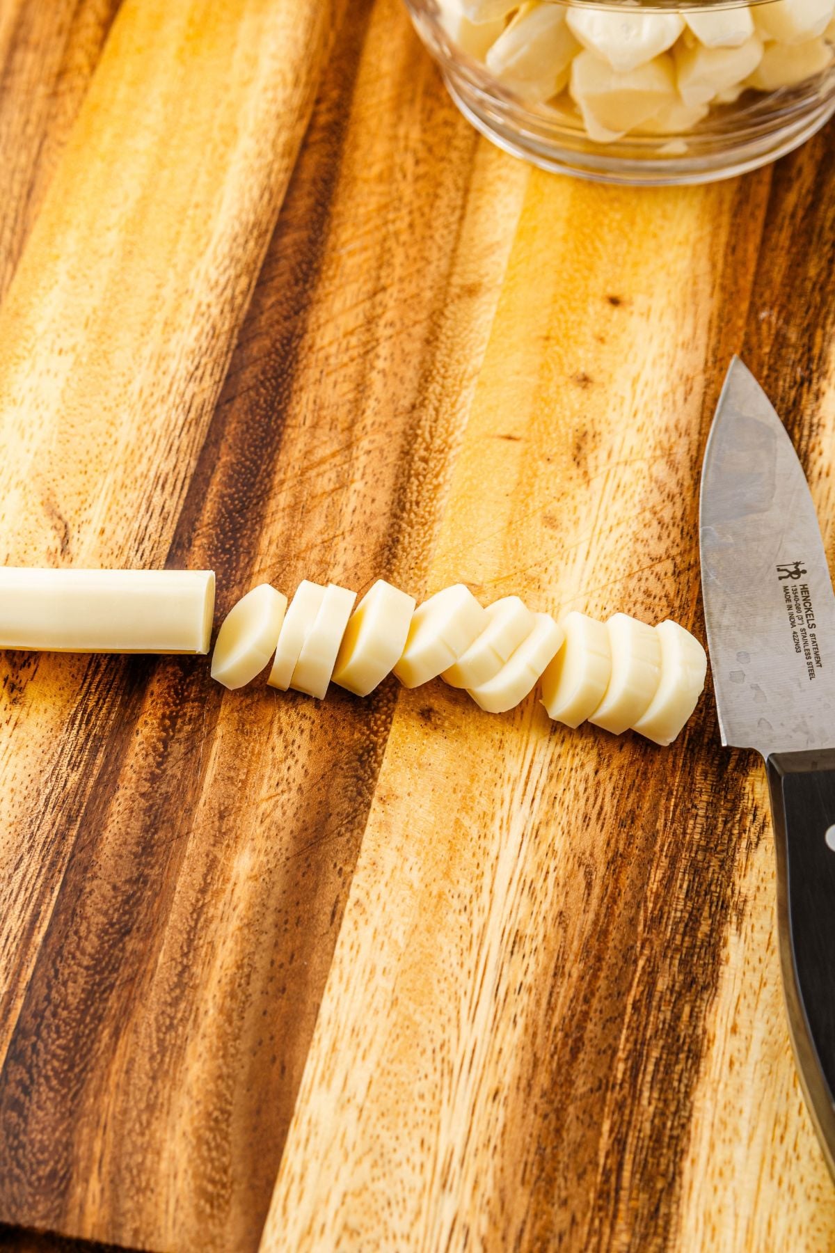 String cheese being cut into small pieces on a wooden cutting board.