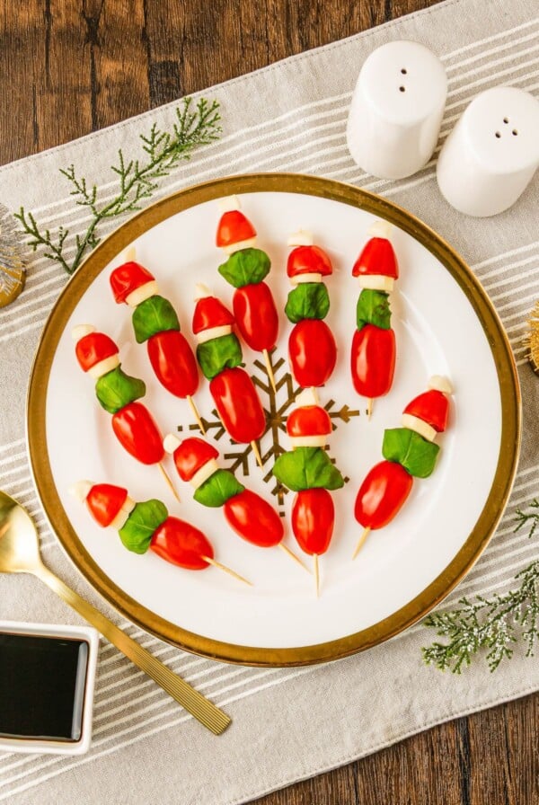Cherry tomato, basil leaves, and mozzarella pieces on wooden skewers on a white plate, with Christmas decor around the table.
