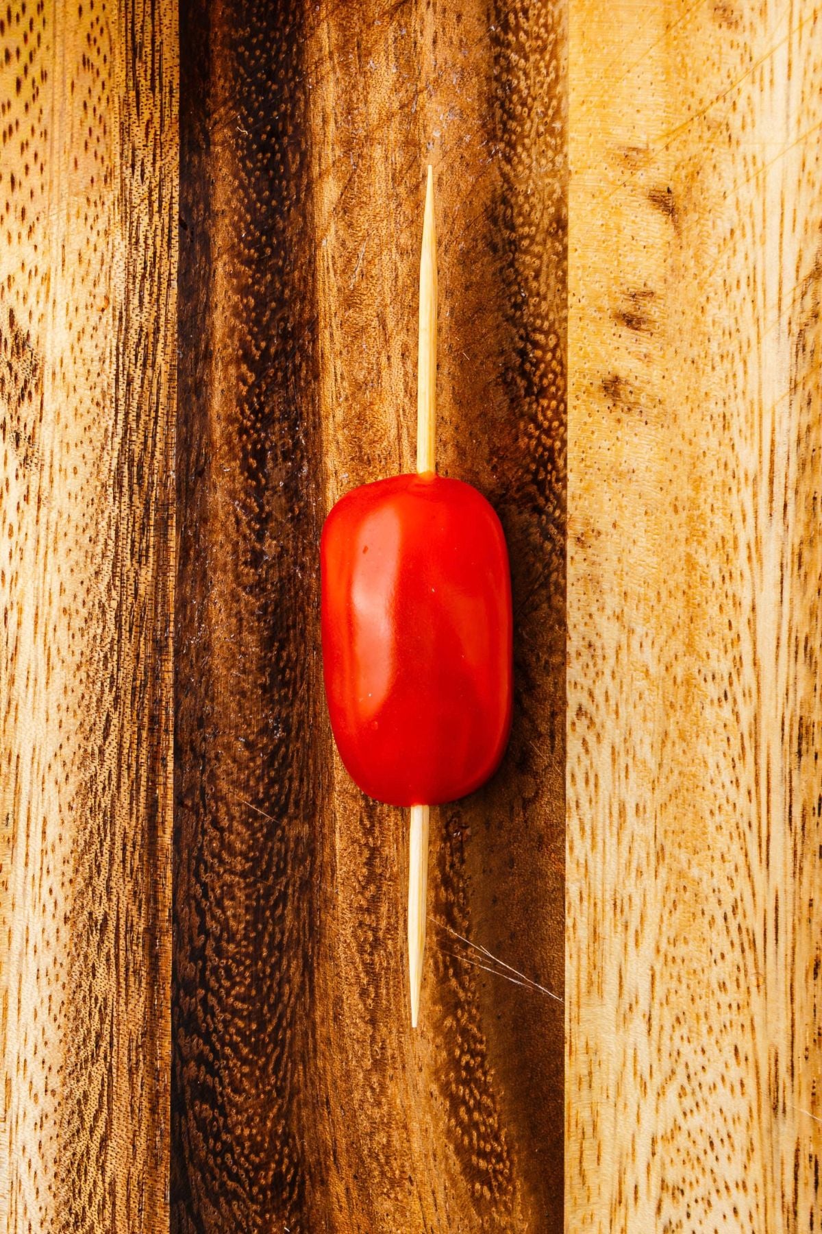 Half of cherry tomato on a skewer, on a wooden cutting board.