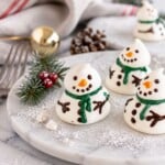 White meringue snowmen on a white plate with holiday decorations around the table.