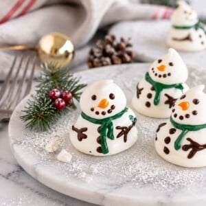 White meringue snowmen on a white plate with holiday decorations around the table.