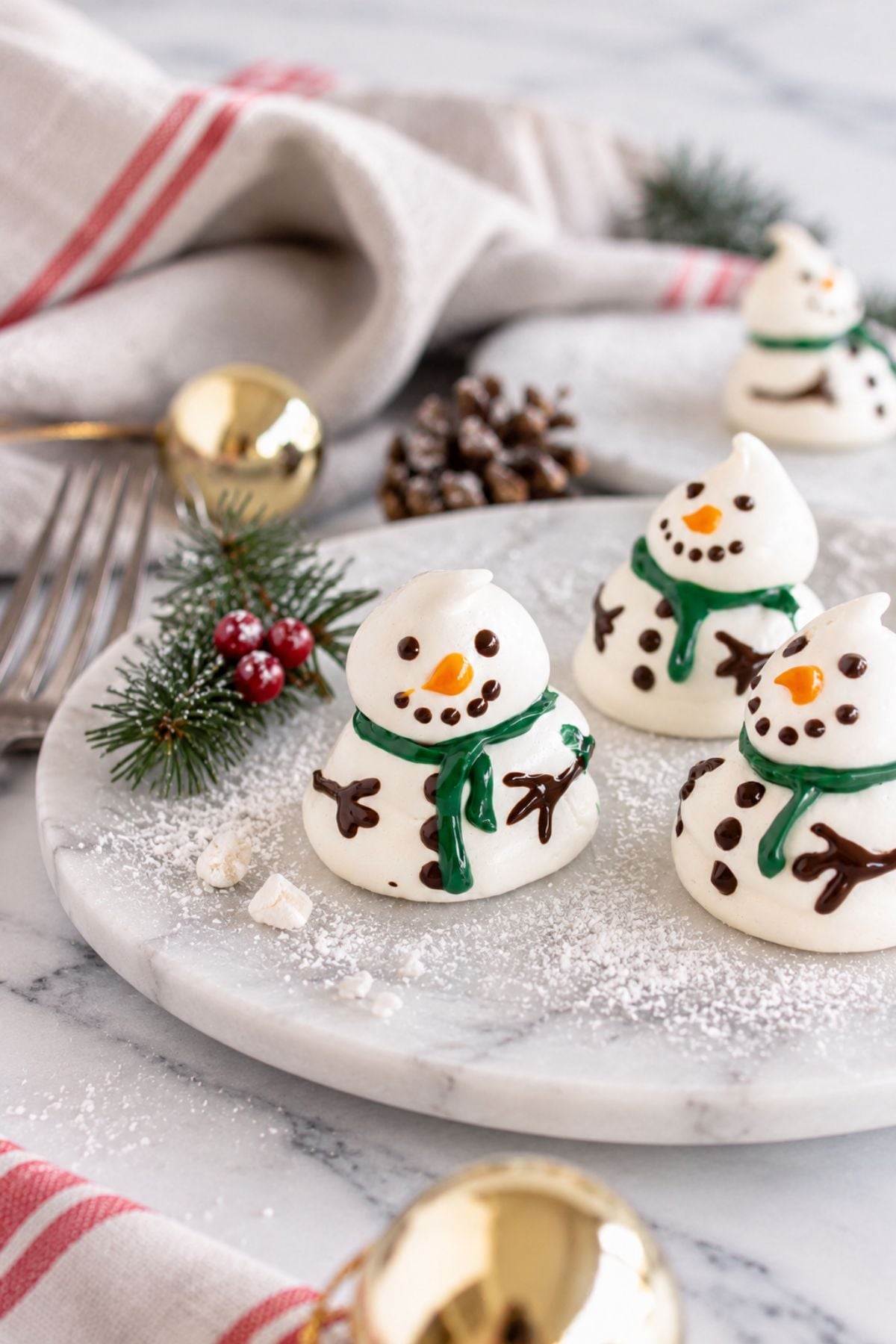 White meringue snowmen on a white plate with holiday decorations around the table.