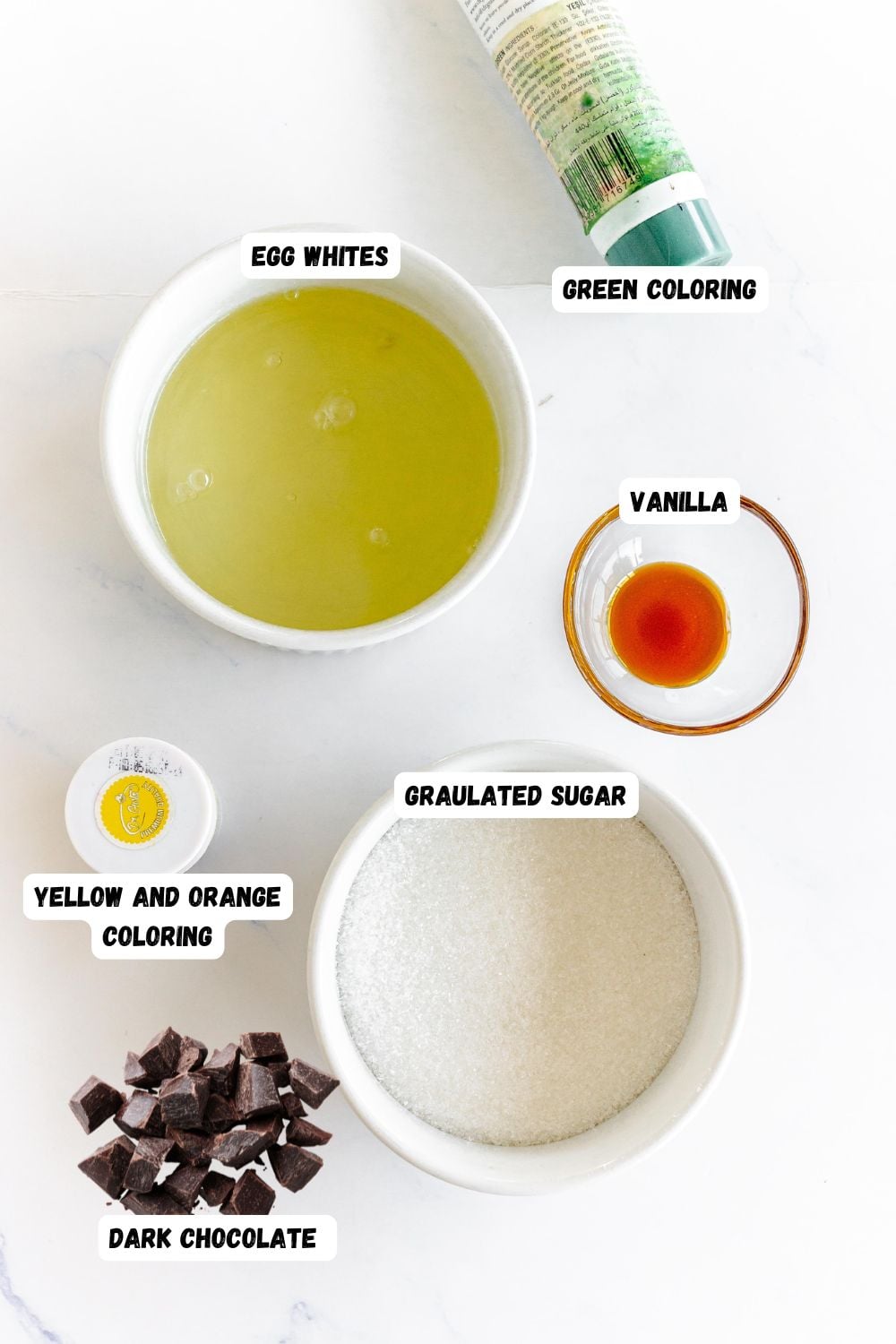 Ingredients needed to make snowman meringues measured into small bowls and labeled on a marble table.