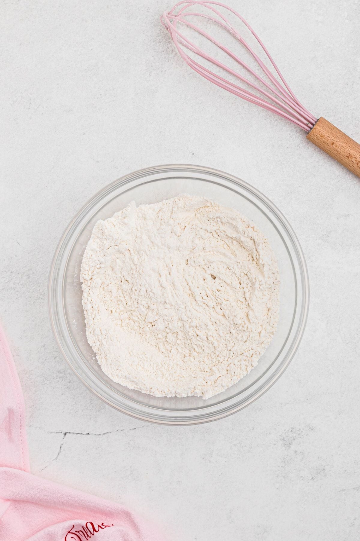 Flour and other dry ingredients mixed together in a large clear glass bowl. 