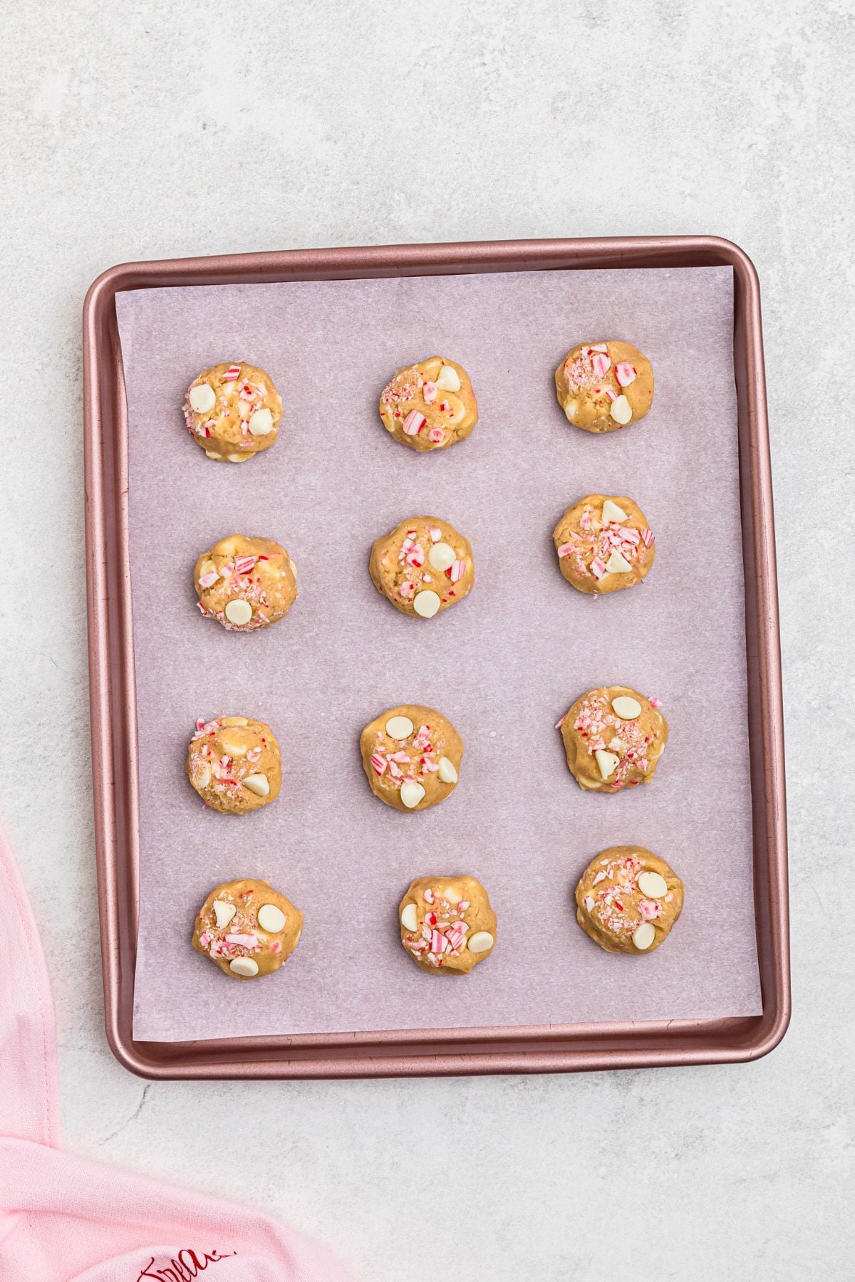 Uncooked balls of dough, on a pink baking sheet lined with parchment paper. 