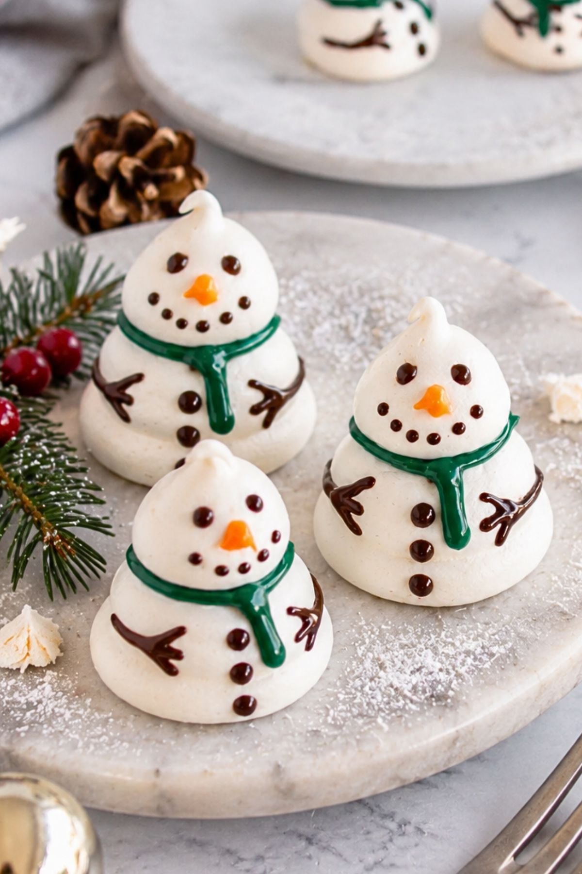 White cookie snowmen on a white plate with holiday decorations around the table.